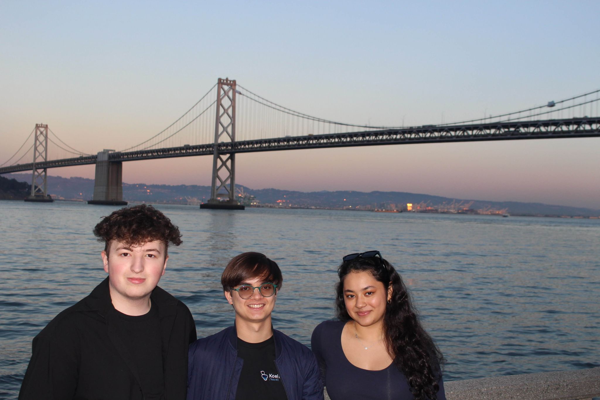 A photo of the Koel Labs founders, Alexander Metzger, Aruna Srivastava, and Ruslan Mukhamedvaleev standing in front of the bay bridge in San Francisco.